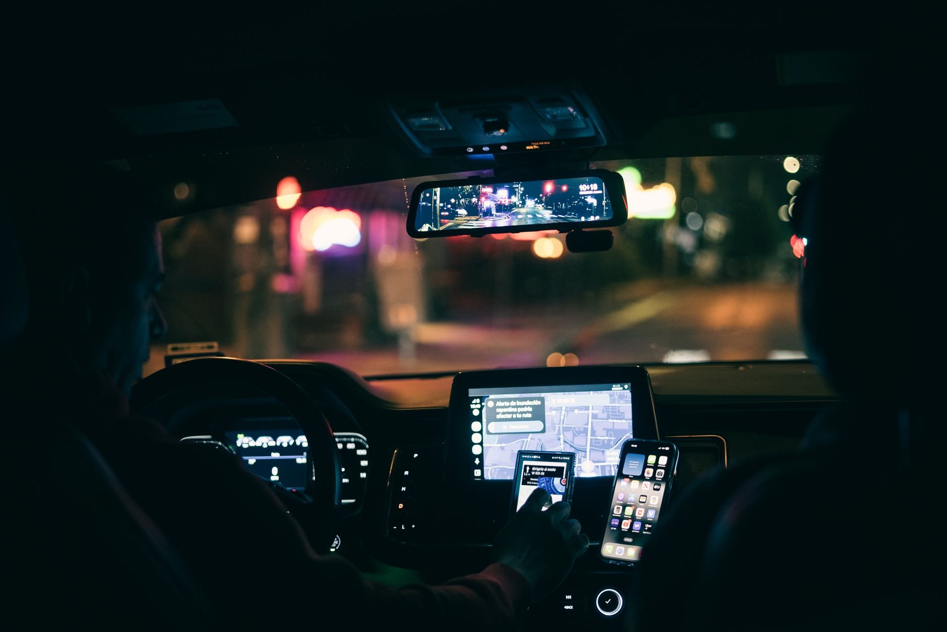 Driver using a smartphone for navigation through city streets at night.