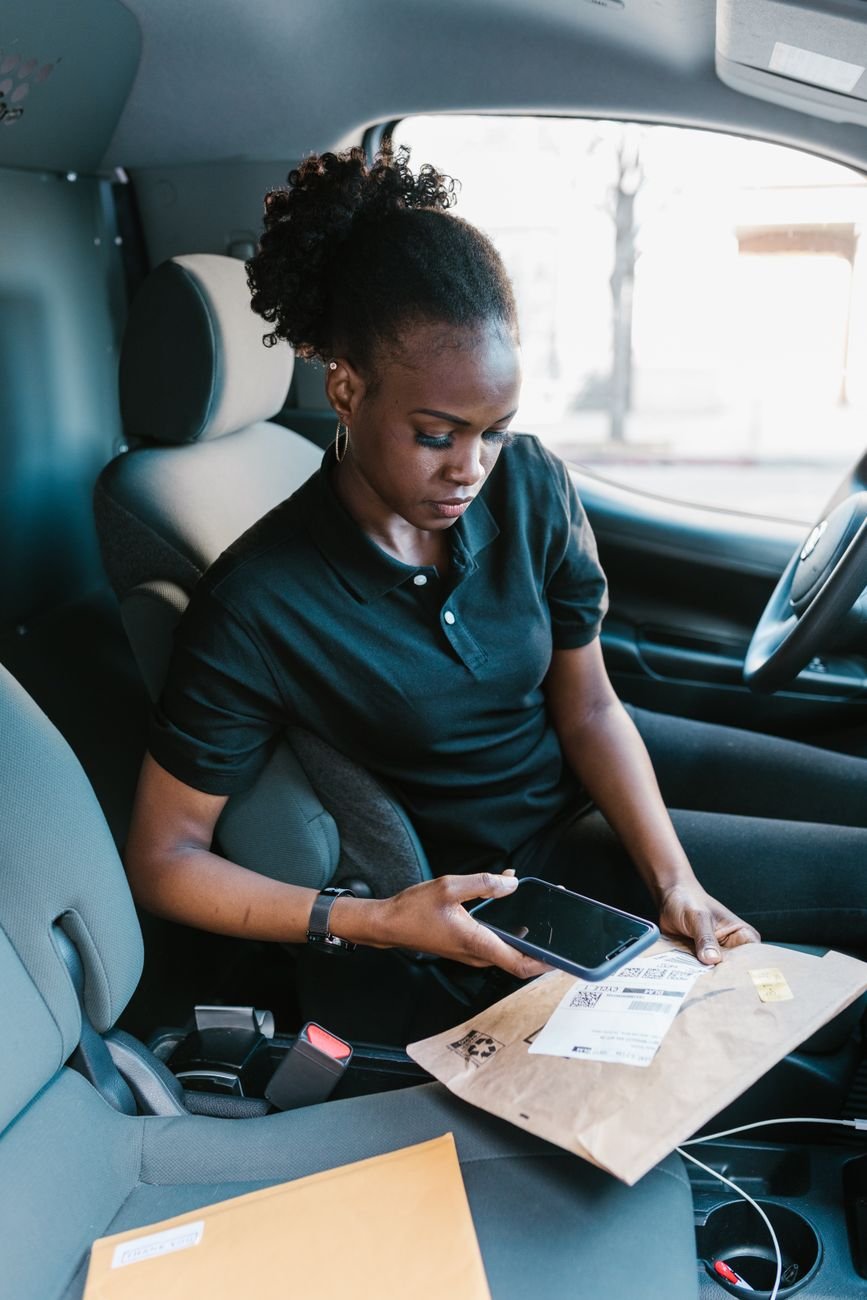 A courier scans a package barcode with a smartphone inside a delivery van.